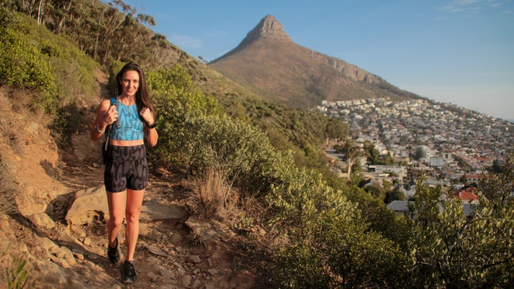 A female hiker on a dirt trail with a mountain and blue sky behind her in South Africa