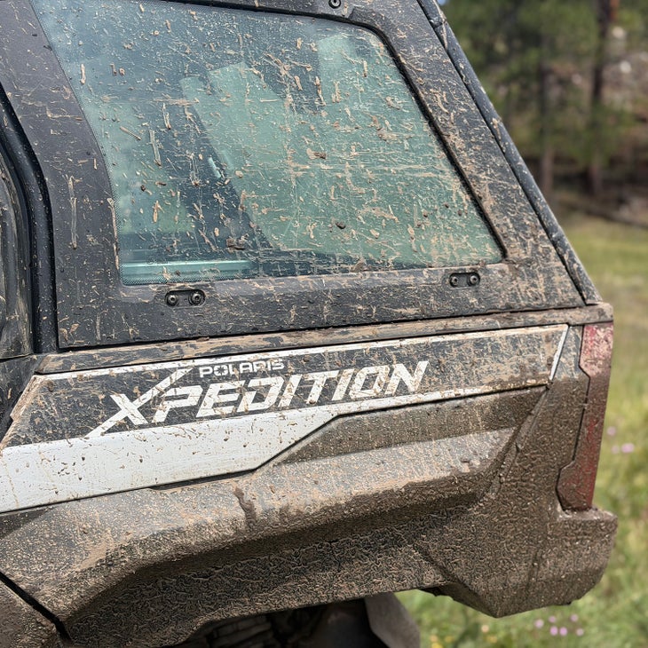 Close-up of the Polaris Xpedition badge on the mud-covered rear panel of the vehicle
