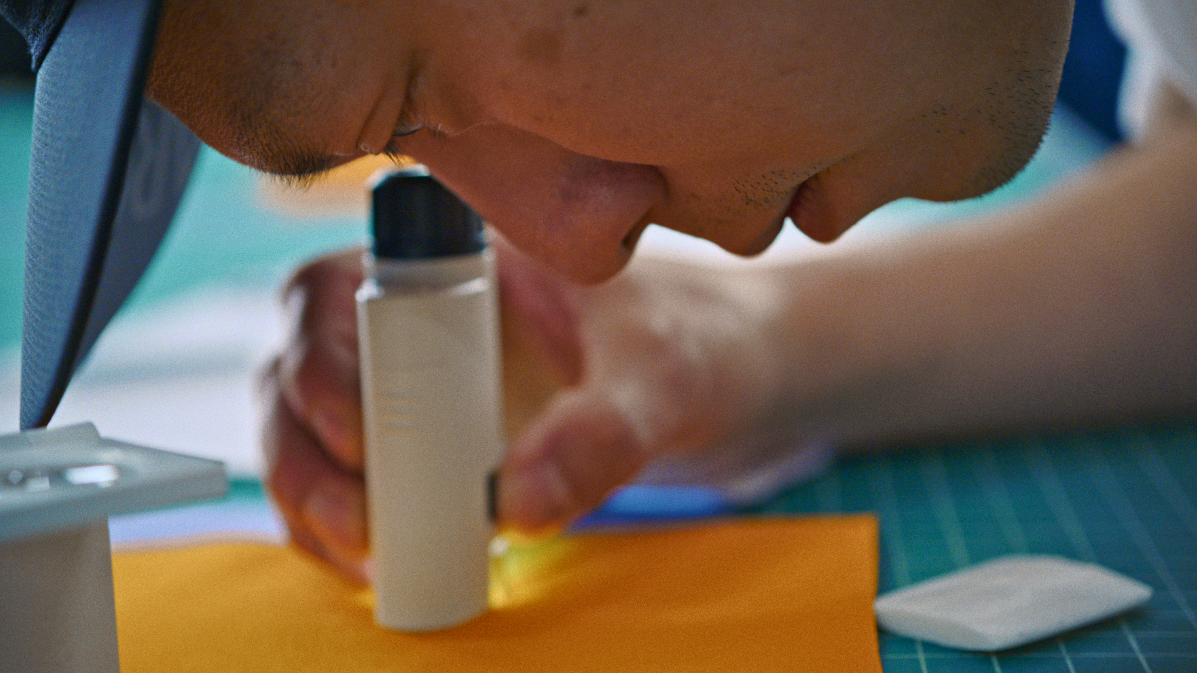 A close-up view of a materials developer using a magnified loupe tool to inspect a bright orange fabric swatch for the Sperro SV jacket.