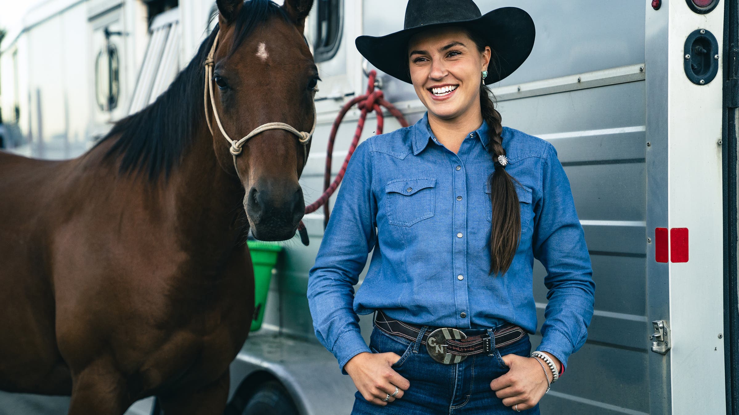 Cowgirl standing with horse displaying custom belt buckle