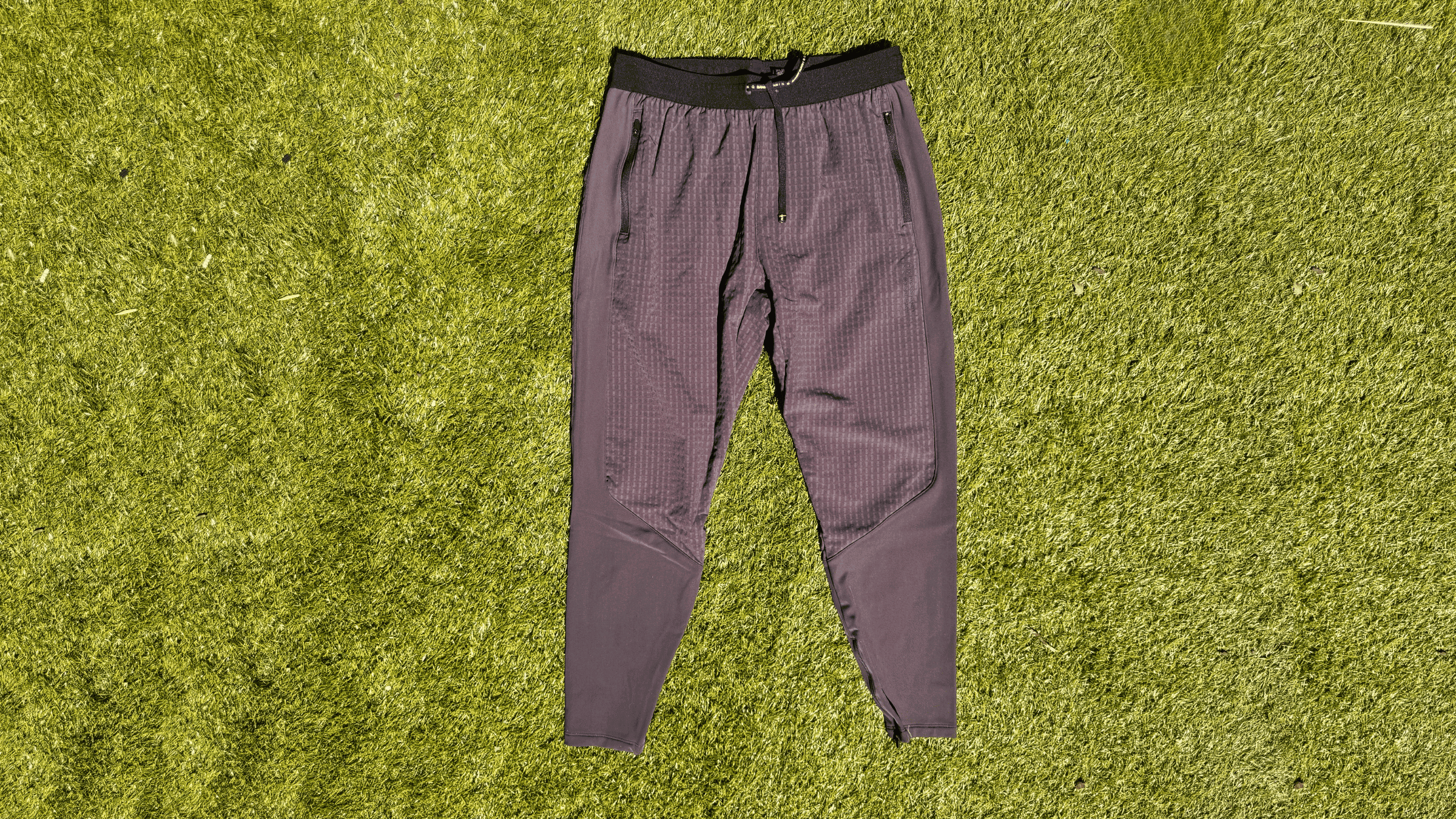 pair of men's dark gray with black waistband Bandit joggers lying flat on green turf