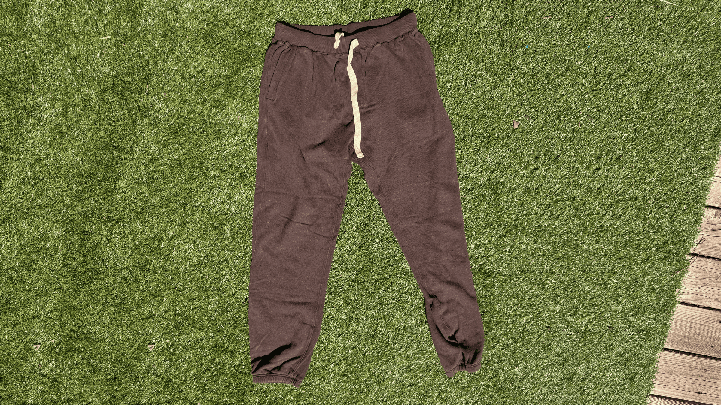 pair of men's dark brown Jungmaven joggers lying flat on green turf in sunlight