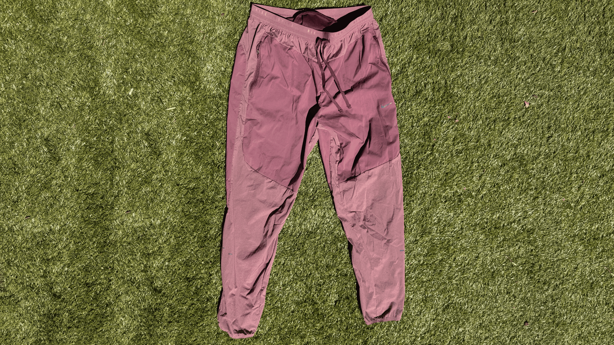 pair of light red men's Nike joggers lying flat on green turf outside