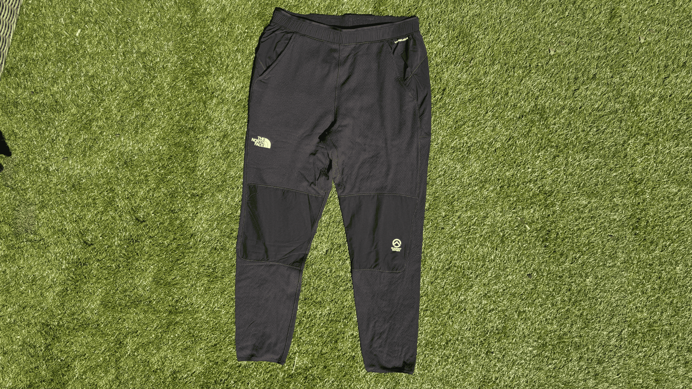 pair of men's black The North Face joggers lying flat on green turf outside in sunlight