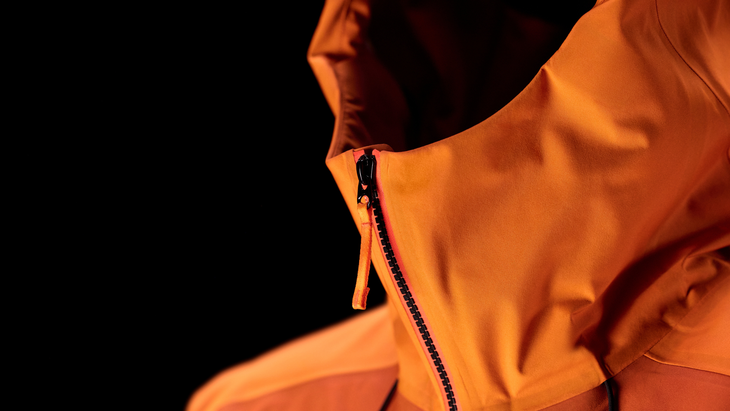 A top-down shot of an orange two-tone Sperro SV jacket laid flat on a grid cutting mat while a designer inspects the central zipper.