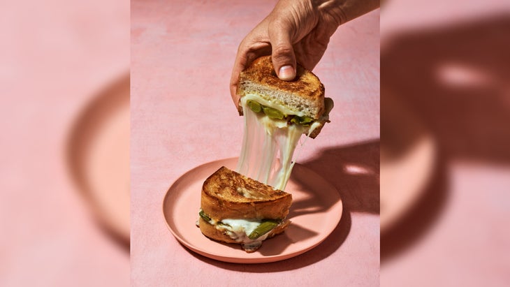 A hand pulling apart a grilled cheese sandwich.