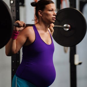 Pregnant woman working out in the gym by doing back squats