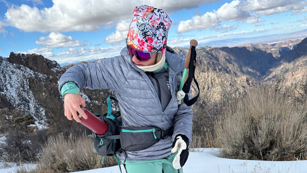Tester wearing grey Black Diamond Deploy Down .5 Pullover Hoody while cross country skiing under bluebird skies