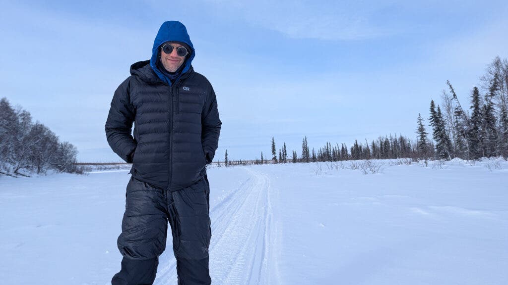 Tester standing at a cold campsite in the snow wearing a black Outdoor Research Helium Down puffy jacket