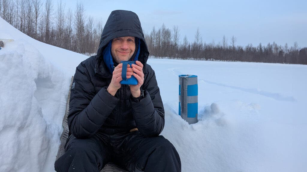 Tester drinking hot chocolate in the snow wearing a black Outdoor Research Helium Down puffy jacket