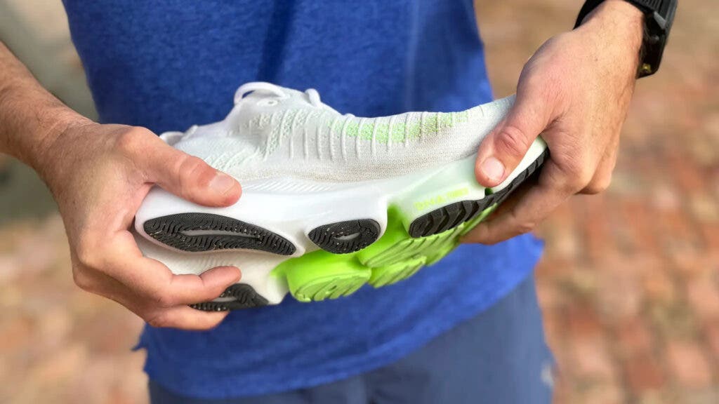 Hands flexing a white Brooks Glycerin Flex running shoe on sale to show its grooved green and black outsole