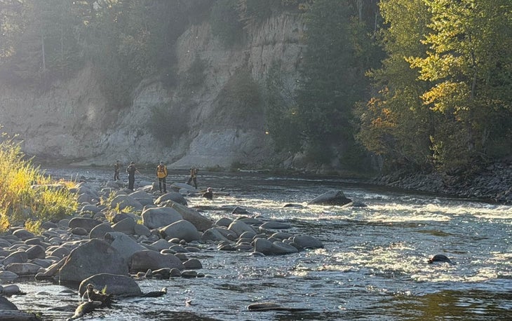 Estacada Fire rescuers stand on rocks and wade through the Clackamas River in Oregon during a rescue of a woman and her dog, Gizmo.