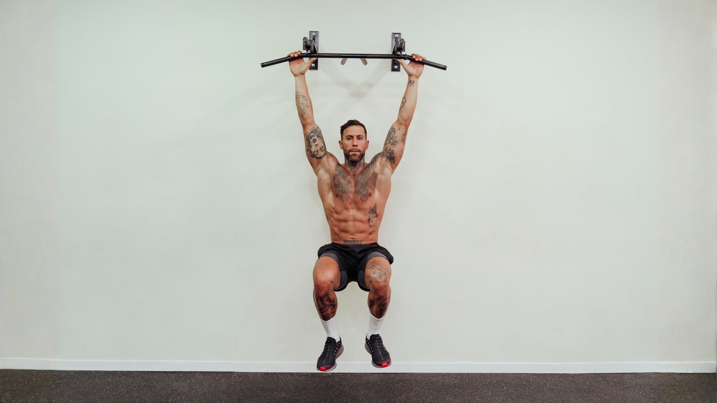 Shirtless sportsman hanging on equipment while exercising in front of wall