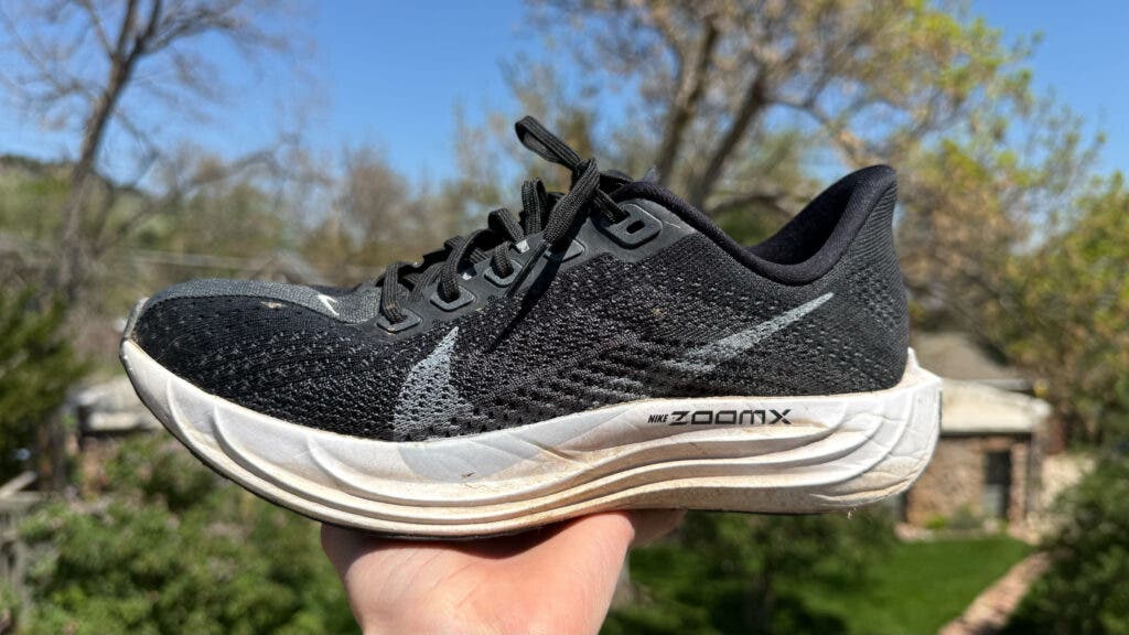Nike Pegasus Plus running shoe on sale, held up in profile to show the black upper and white ZoomX midsole