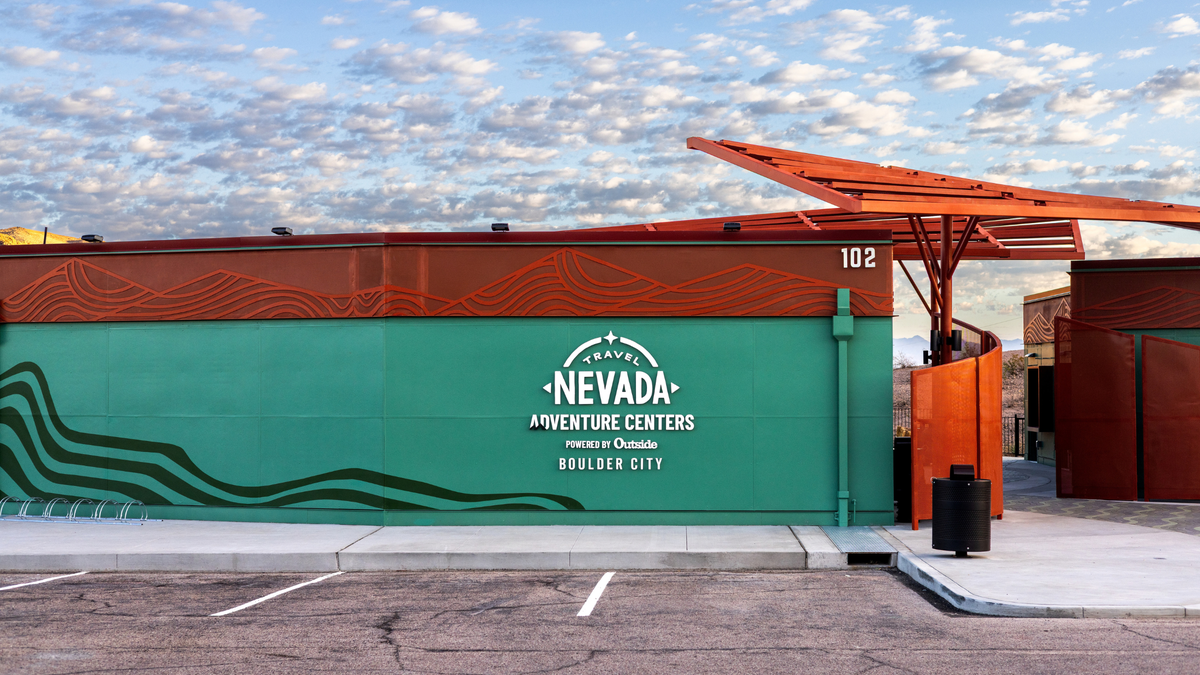 Front of the green Travel Nevada Adventure Centers building in Boulder City with orange steel shade structures and a parking lot