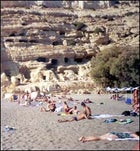 Sun worshippers lounge on Matala's protected beach, in front of caves used as ancient Roman tombs and Minoan storage cells.