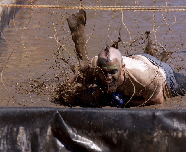 A participant crawls under live wires during a Tough Mudder event.