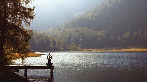 woman meditating on a lake with the best meditation apps