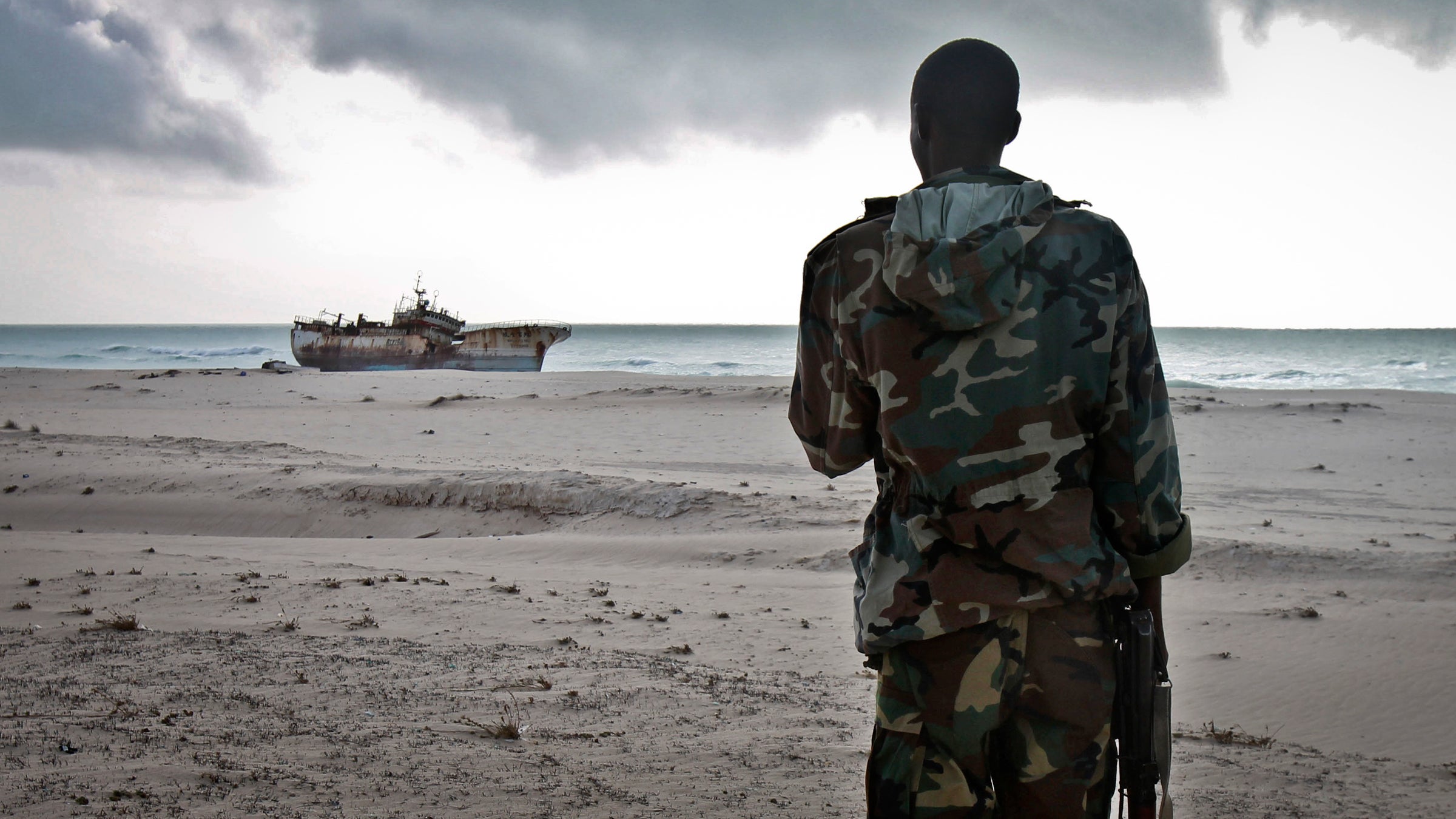 A Somali soldier looks out at a Taiwanese fishing vessel that washed up on shore after the pirates were paid a ransom and released the crew, in the once-bustling pirate den of Hobyo, Somalia.