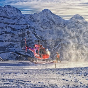 Switzerland alps mountain winter swiss helicopter aviation landing rock resort ski Maennlichen jungfrau peak highland holidays snow flakes flare sunlight slope sunshine red white blue activity serviceman vacation vessel vehicle flight