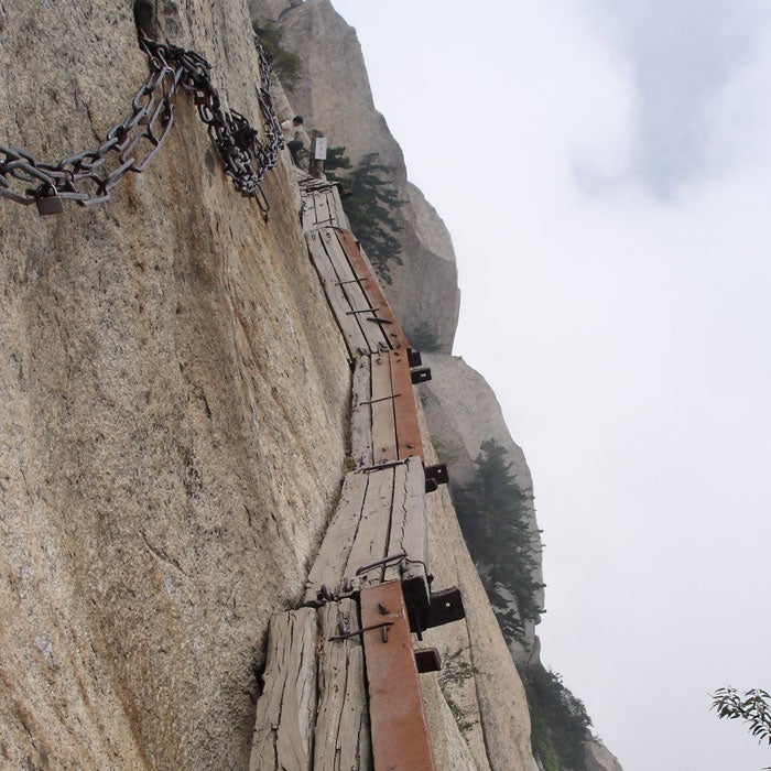 Pilgrims have climbed to the temples on the five spires of Mount Hua Shan for centuries. Almost all of the climbs are treacherous, with nearly vertical stairways and few handholds. However, the plank trail to the South Mountain is a different story. Called the most dangerous hike in the world, it consists of wooden platforms bolted onto the mountainside.
Trekkers need to hook into an iron chain paralleling the boards, which hover thousands of feet above the ground. Even getting to the trail is difficult and includes a climb up a vertical rebar staircase. At one point, the planks disappear entirely and hikers must use small divots carved into the rock. There are no official death statistics, but the rumor is that 100 people per year die on Hua Shan. Multiply that over centuries and it may be the deadliest peak in the world.