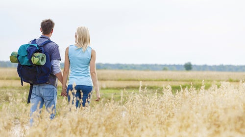 Rear view of young hiking couple walking through field