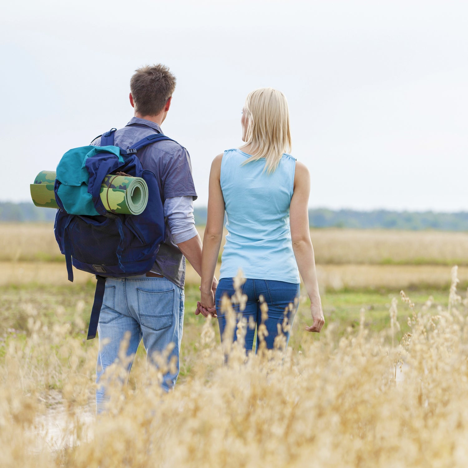 Rear view of young hiking couple walking through field