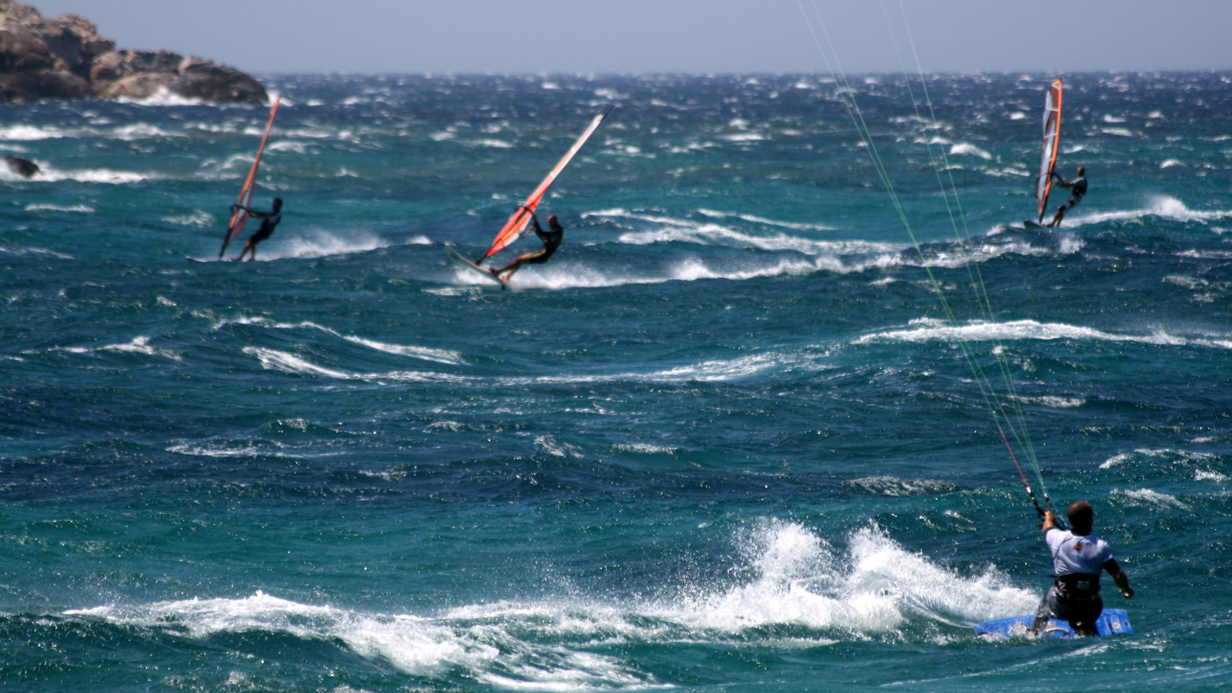 multiple people windsurf off the coast of greek islands on a windy day